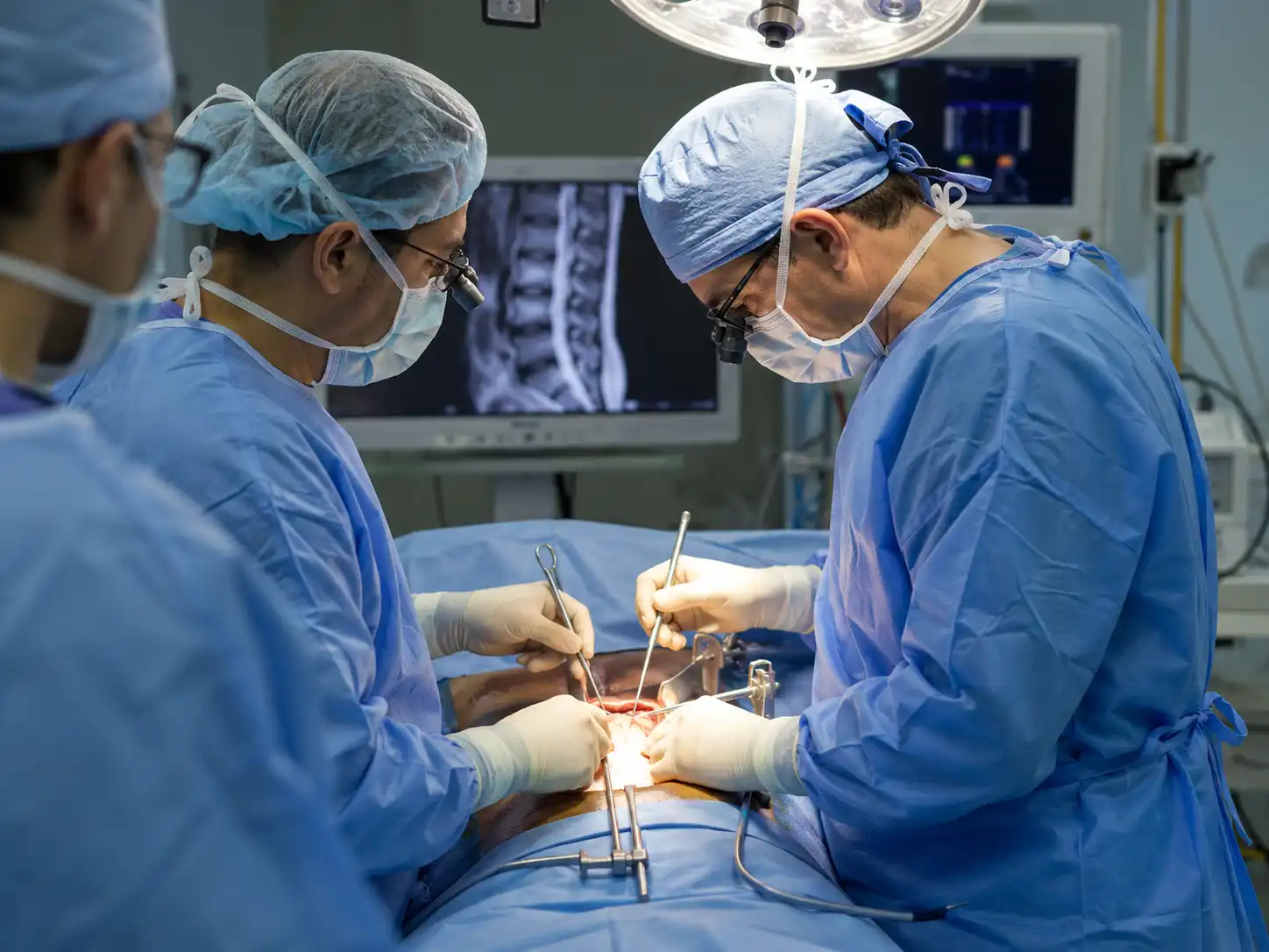 Surgeon performing spine surgery with imaging in the background